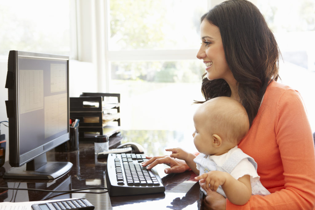 eine Frau sitzt am Computer, mit ihrem Baby auf dem Schoß